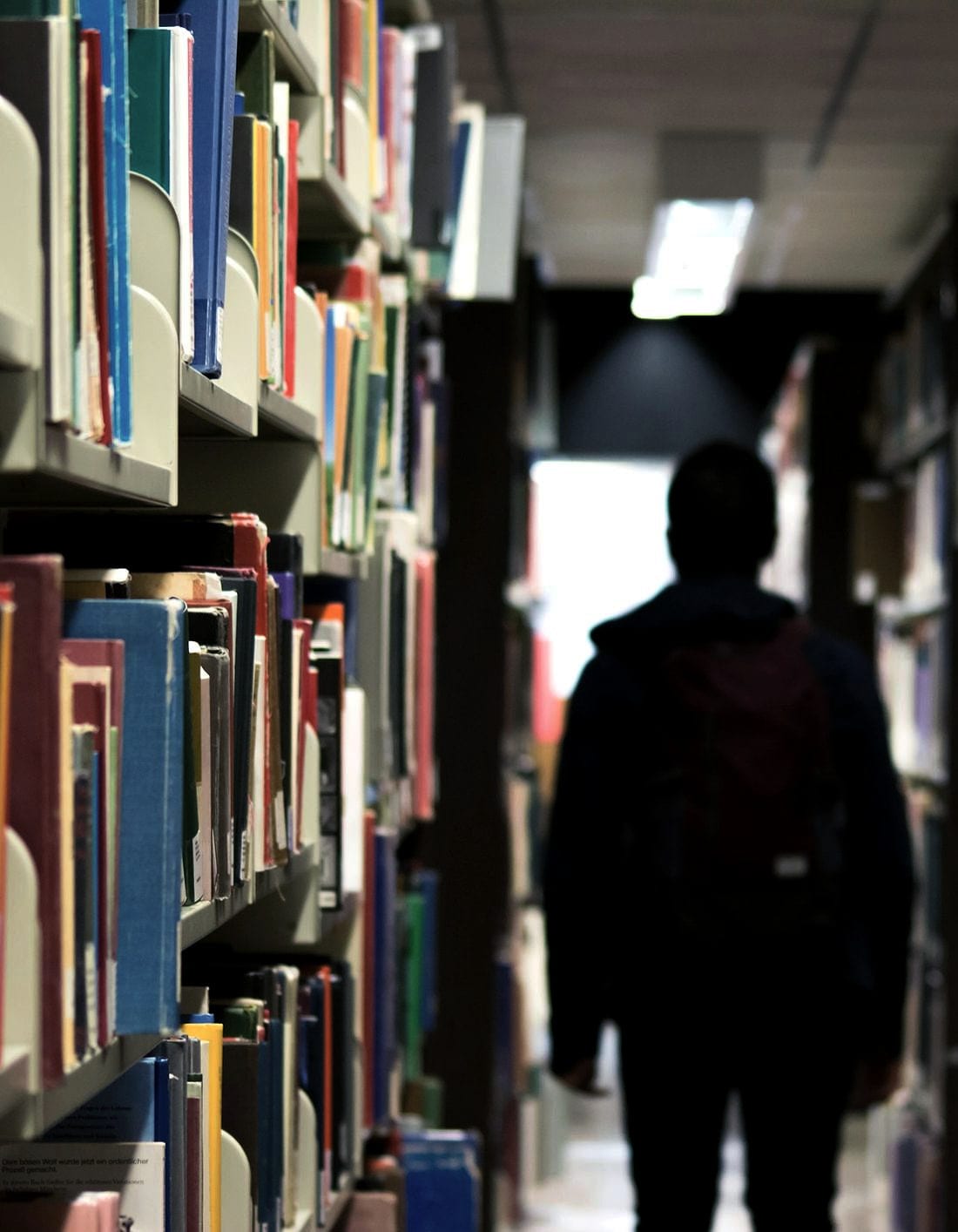 A student walking a library aisle between full shelves