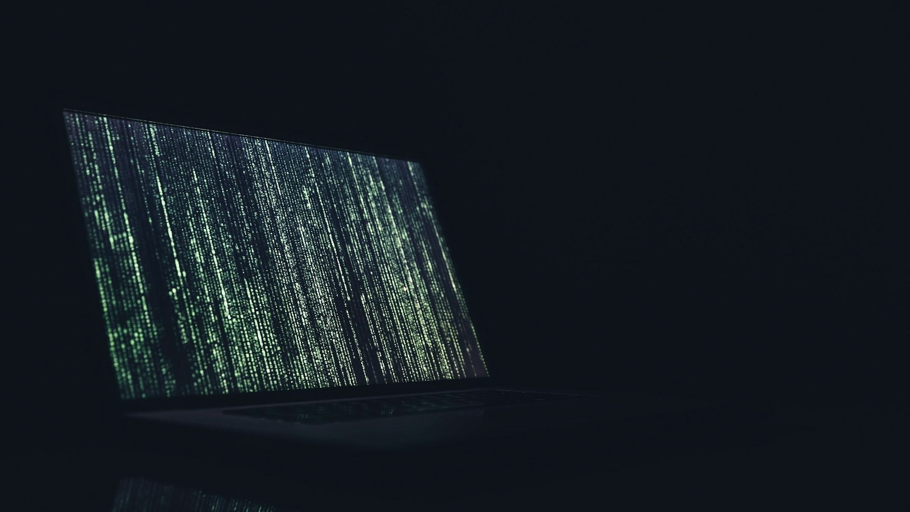A laptop open in the dark with characters streaming down the display