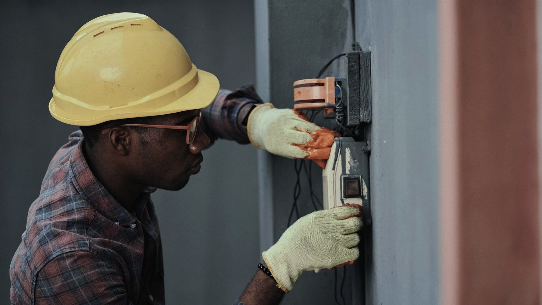 An electrician in a hard hat working on a wall panel