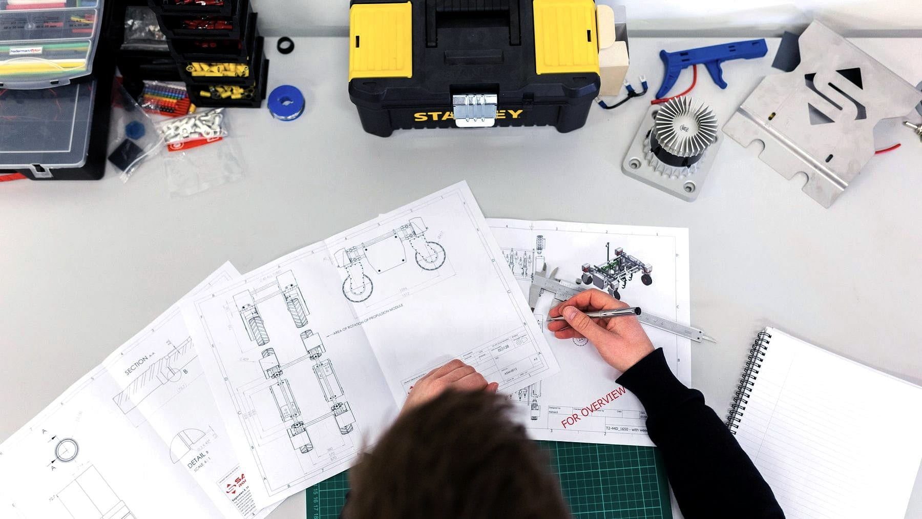 Someone drawing out a schematic on a bench beside their tools