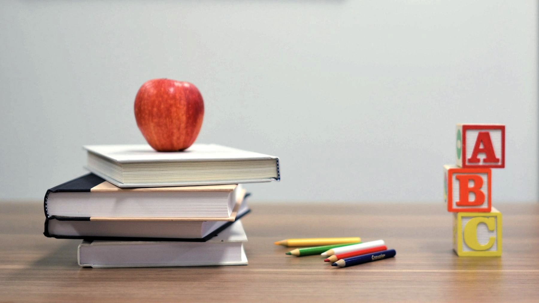 Schoolbooks stacked beside lettered blocks and an apple