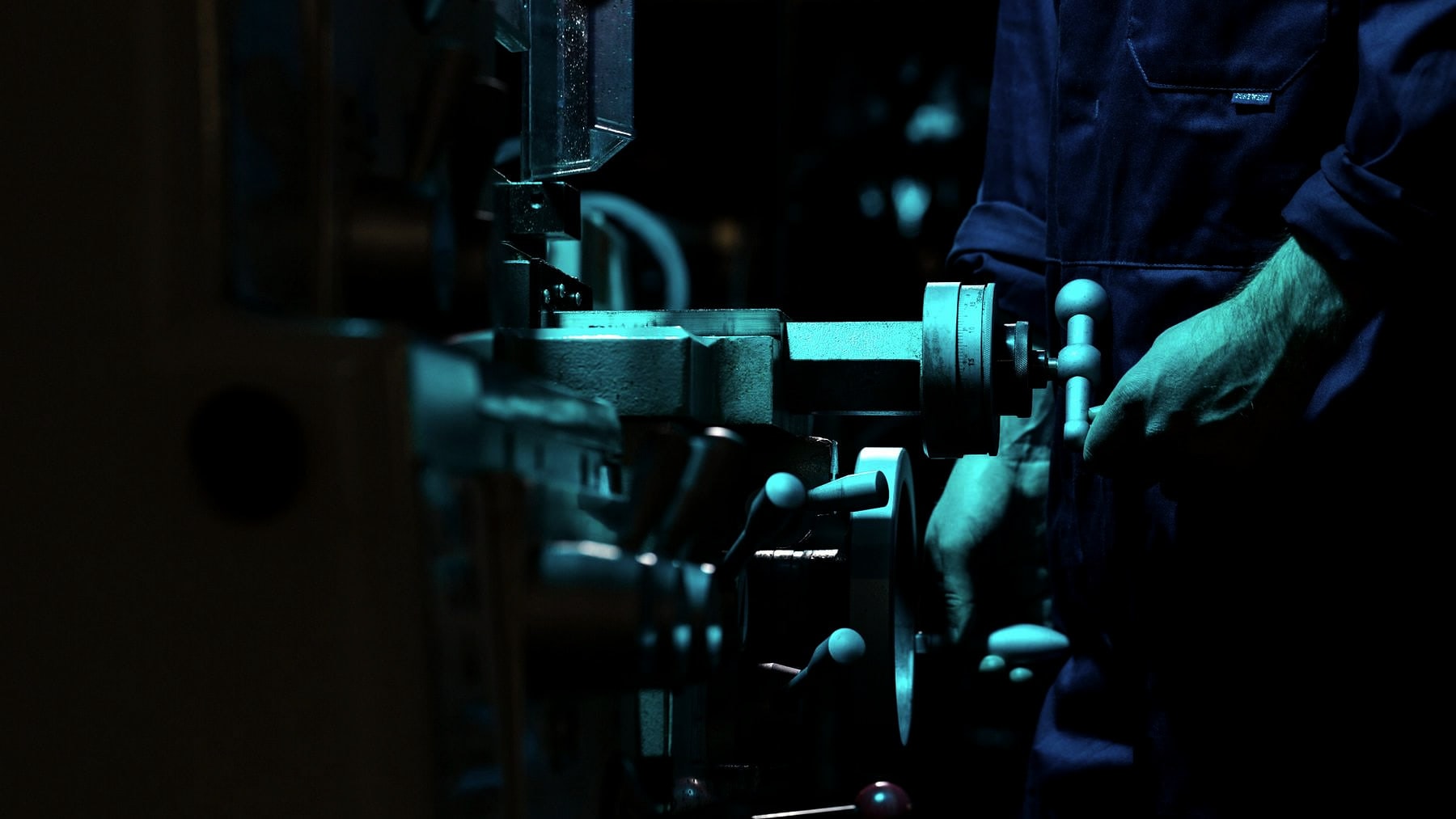 Gloved hands setting work in a machine under teal light
