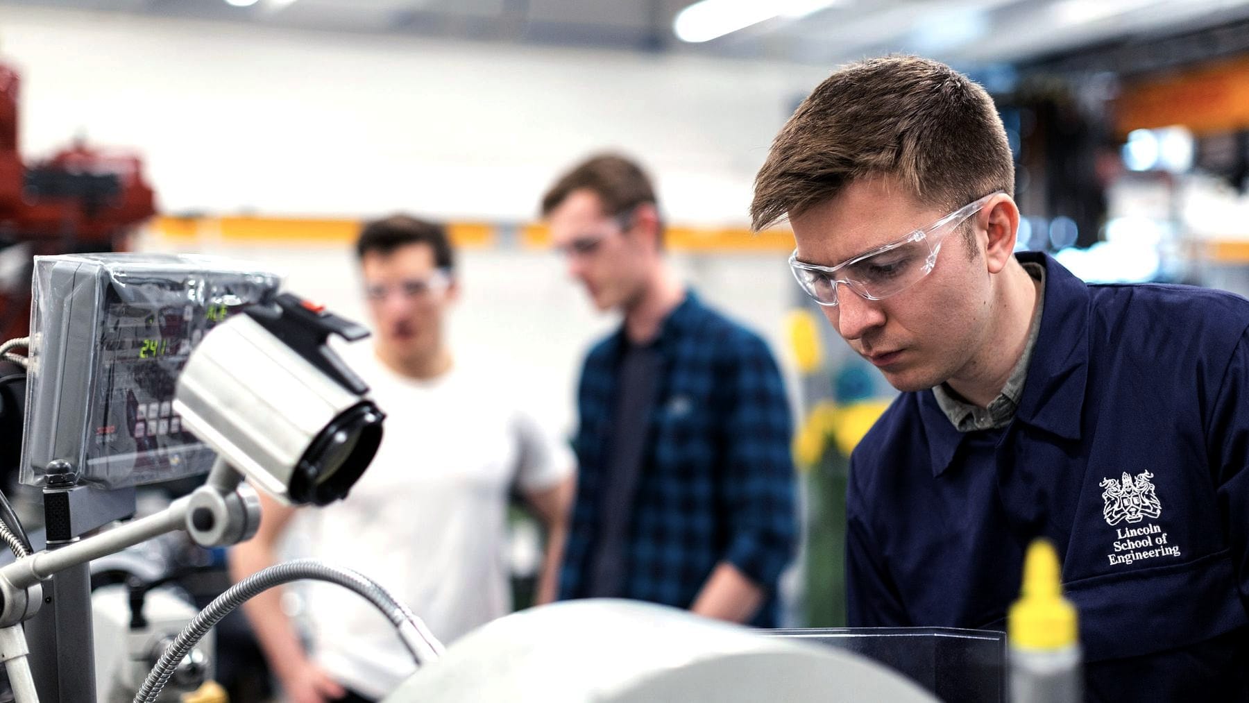 Three people in safety glasses working around a shop machine