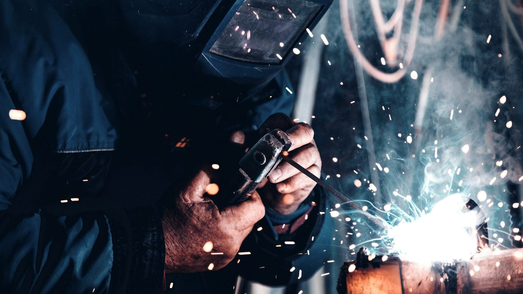A welder working a joint with sparks thrown across the frame