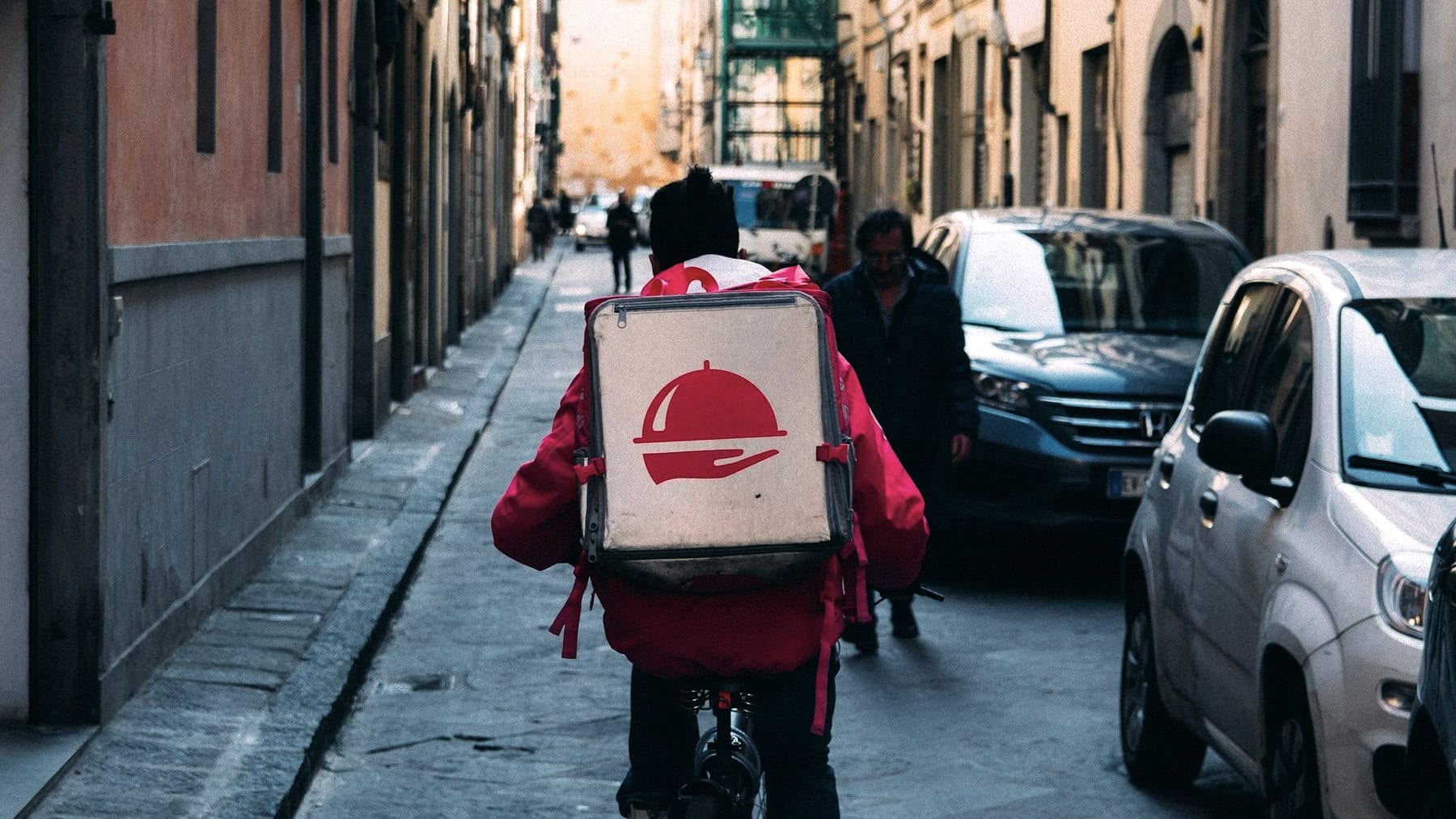 A courier riding a delivery box through a narrow street