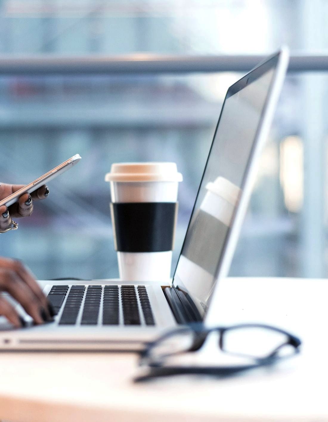 A hand marking up a phone beside a laptop and a coffee