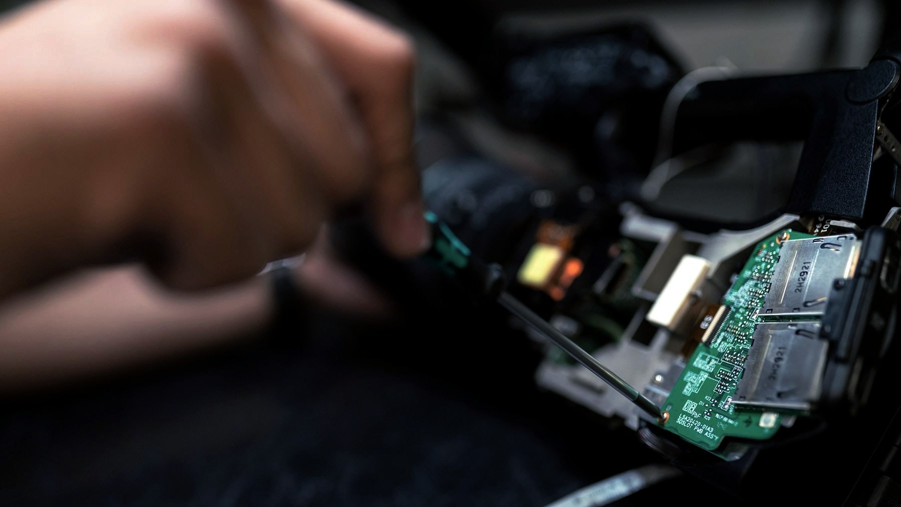 Hands working a circuit board with tweezers under close light