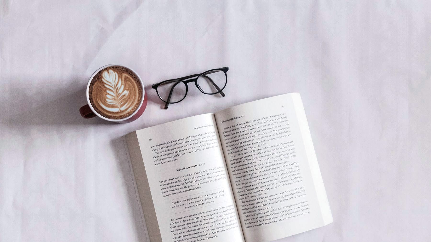 An open book lying beside a coffee and a pair of glasses